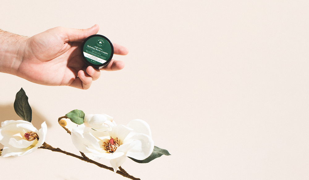 Magnolia League moisturizer being held with magnolia flower in background